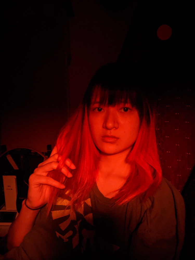 me with died red hair and straight bangs in a zelda shirt red lighting